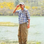 Aflah, the best freelance digital marketer in Tirur, wearing a blue checkered shirt, cap, and beige pants standing near a lake.