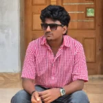 Aflah, a digital marketer in Kannur, sitting in front of a traditional wooden door wearing a red checkered shirt and sunglasses