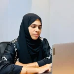 Woman wearing a black hijab and black embroidered outfit working on a Lenovo laptop at a desk